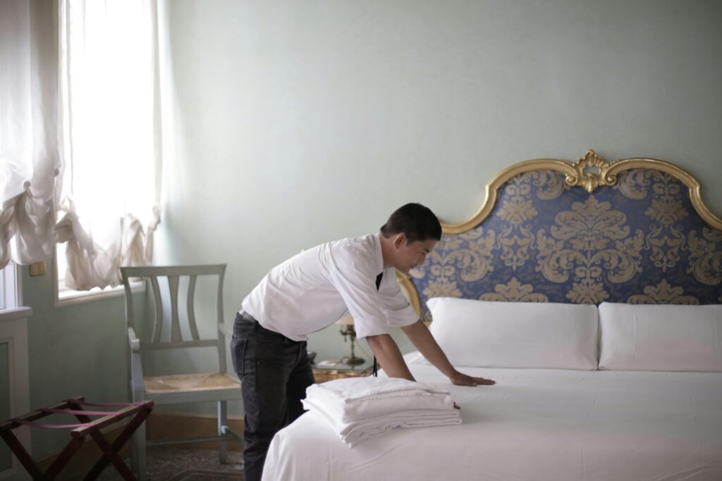 A hotel employee in a luxury room adjusting bed linens, creating a welcoming atmosphere.