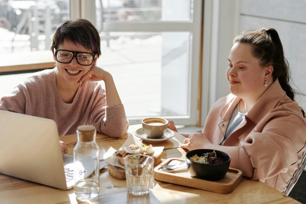 Two cheerful women enjoying coffee and food in a bright, modern indoor setting.