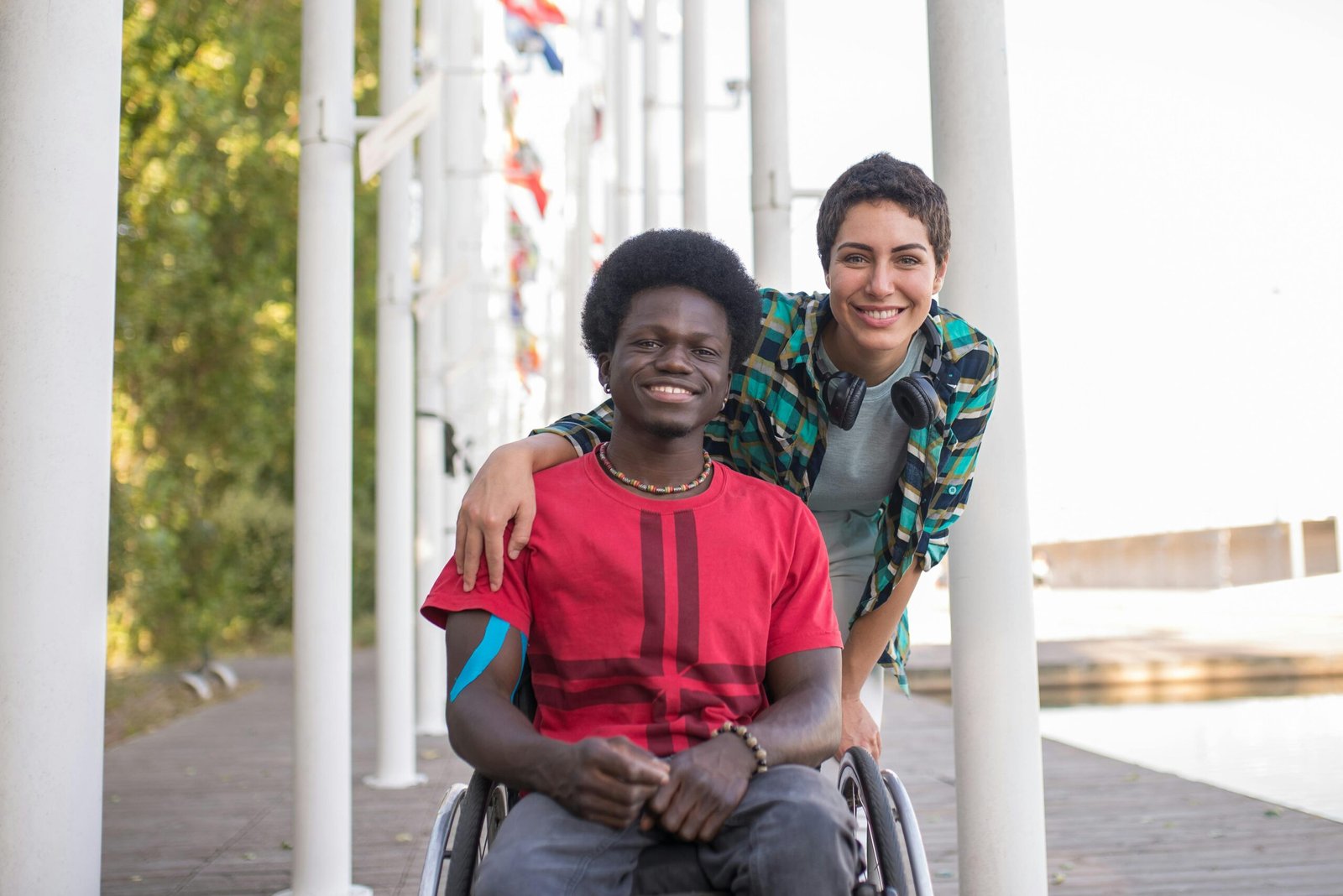 Two friends, one in a wheelchair, smiling outdoors in Portugal. Embracing diversity and friendship.